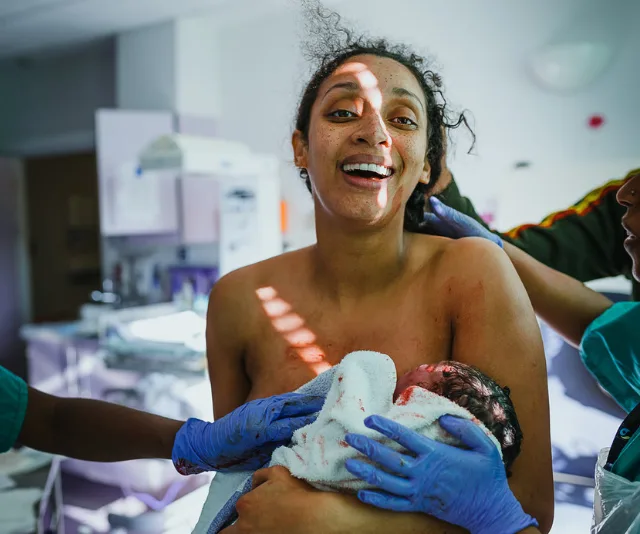A joyful mother holds her newborn baby, surrounded by medical staff in a hospital delivery room.