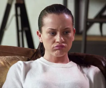 Woman on a couch, looking upset or thoughtful, in a brown leather chair.