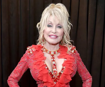 Dolly Parton smiling in a red embellished dress at the 2019 Grammy Awards.