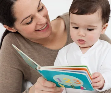 "Smiling adult and baby reading a colorful book with numbers."