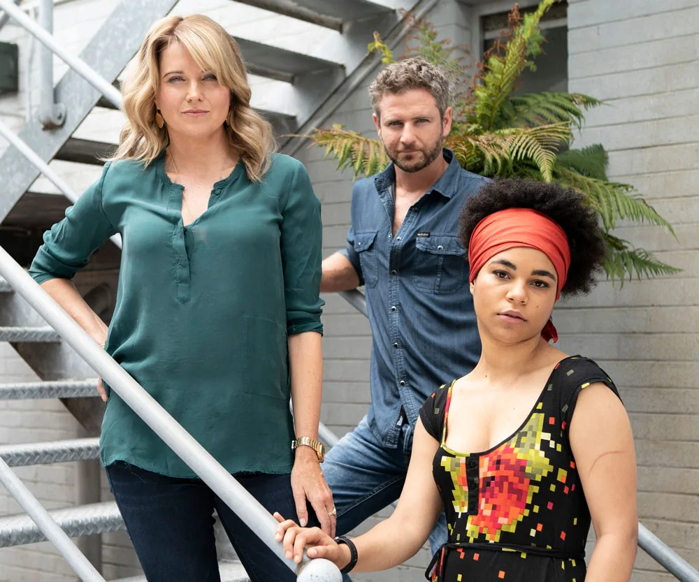 Three characters from "My Life is Murder" stand on stairs; casual attire, urban setting.