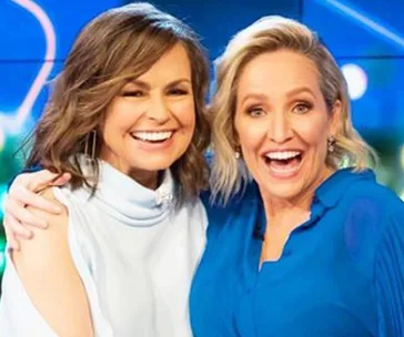 Two women smiling and posing together, one in a white top and the other in a blue dress.