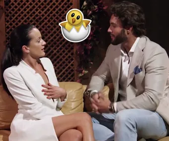 A man and woman in formal attire sit on a couch talking; a cartoon chick in an egg overlays the image.