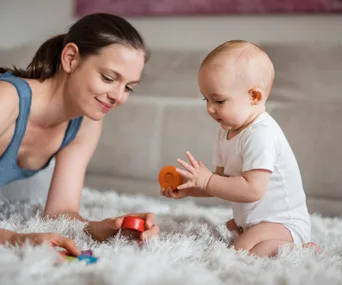 A mother and baby on a soft rug, playing with colorful eco-friendly toys together.