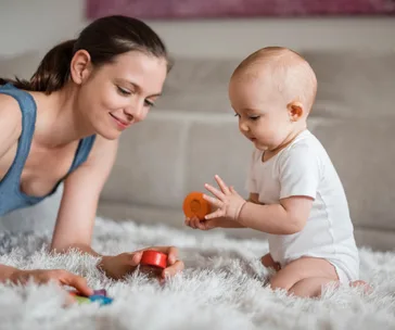 A mother and baby on a soft rug, playing with colorful eco-friendly toys together.