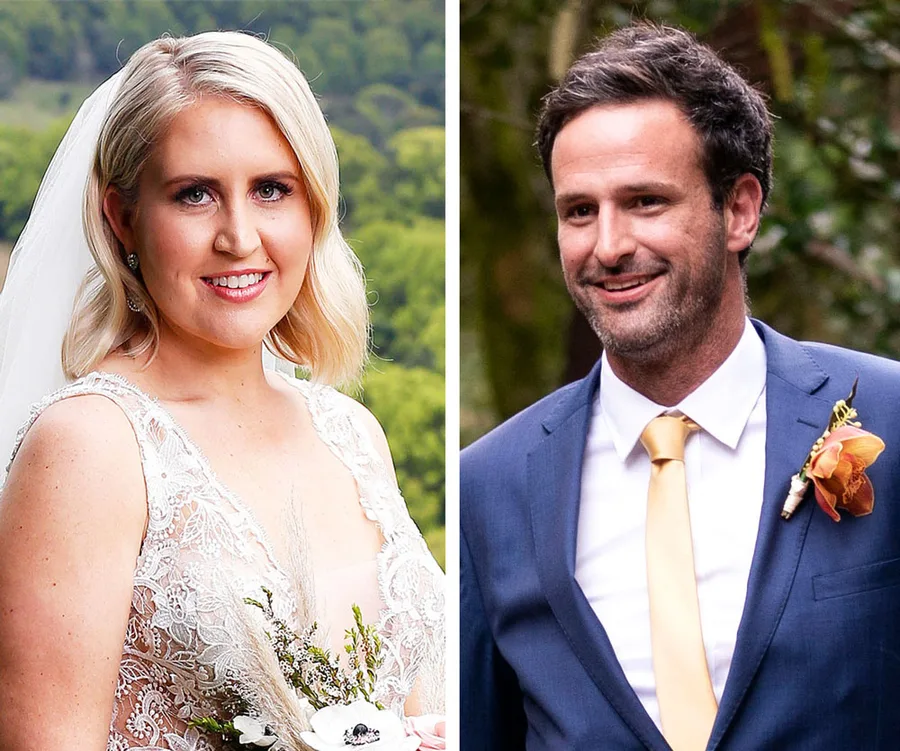 Bride in lace wedding dress holding bouquet and groom in suit with orange boutonnière, outdoors background.