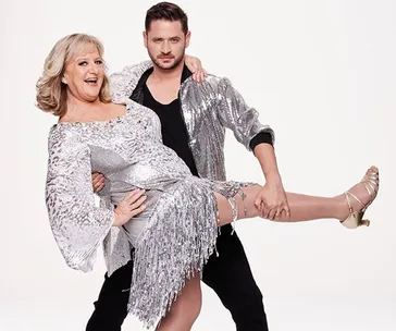 Dancing couple in glittery costumes, with one partner holding the other mid-dance.