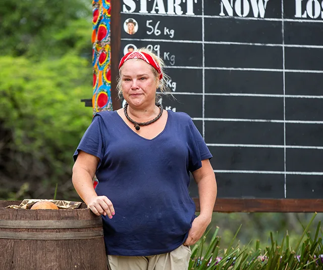 Woman in a blue shirt with a red bandana stands near a weight chart in an outdoor setting.
