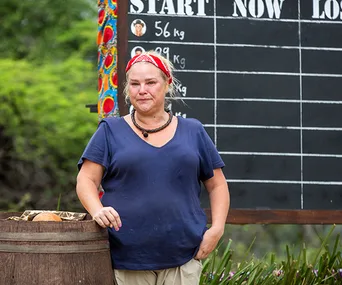 Woman in a blue shirt with a red bandana stands near a weight chart in an outdoor setting.