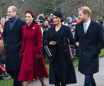 Royal couples walking outside, dressed in formal winter attire, with a crowd behind them.