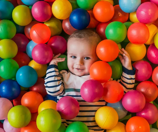 Baby smiling in a colorful ball pit, surrounded by multicolored plastic balls.
