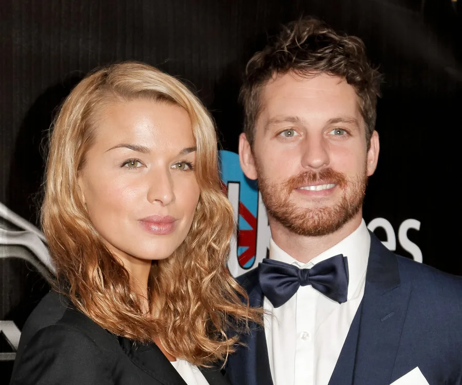 Couple posing together on the red carpet, woman with wavy hair and man in a bow tie and suit.