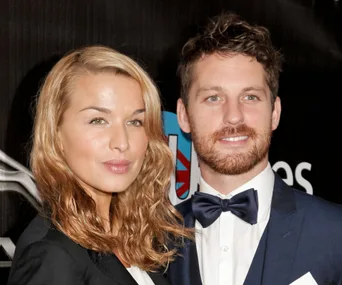 Couple posing together on the red carpet, woman with wavy hair and man in a bow tie and suit.