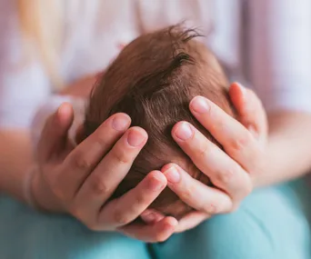Hands gently cradling a newborn baby's head.