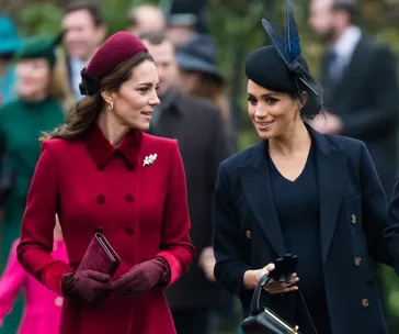 Two women in elegant outfits, one in burgundy and one in navy, walking outdoors and engaged in conversation.