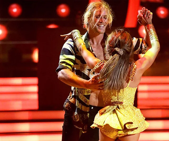 Man and woman dancing energetically on a stage with bright lights in the background.