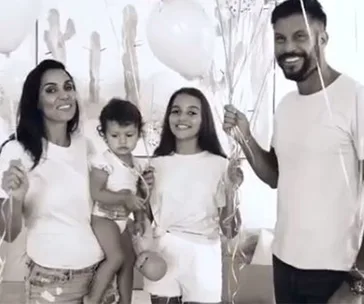 A family of four smiling, holding balloons in a festive setting.