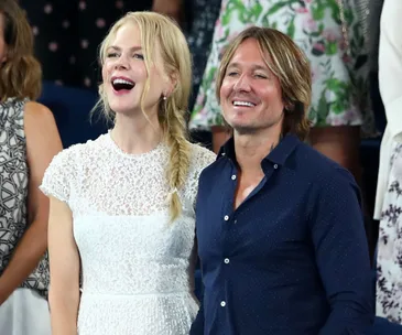 Two people smiling and standing together at an event, surrounded by others in the background.