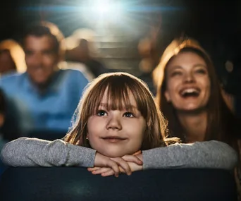 Child and parents enjoying a movie at a cinema, with light from the screen illuminating their faces.