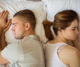 Man and woman in bed facing away from each other, appearing upset or distant.