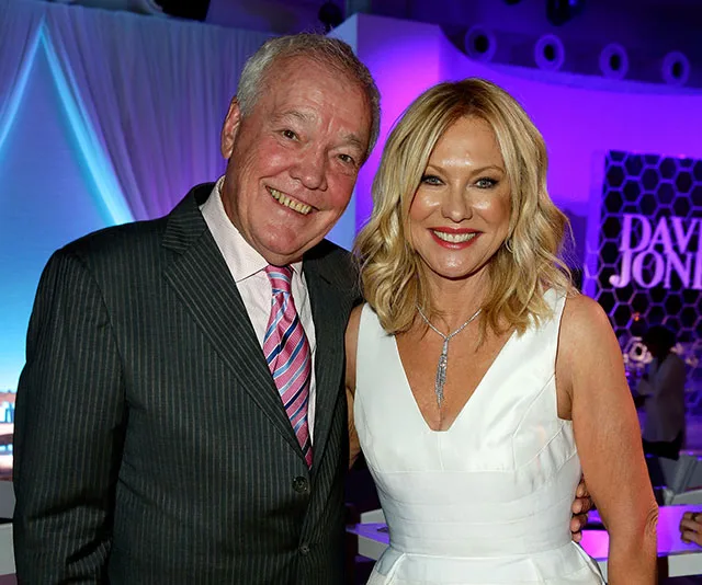 A smiling couple poses together in formal attire at an event with ambient lighting.