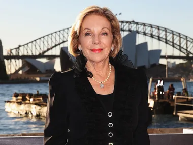 An individual smiling in front of Sydney Opera House and Harbour Bridge during sunset.