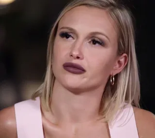 Young woman with blonde hair and hoop earrings, wearing a pink top, appears deep in thought.