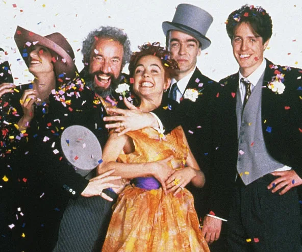 Group of people celebrating with confetti, likely from "Four Weddings and a Funeral," wearing formal attire and smiling.