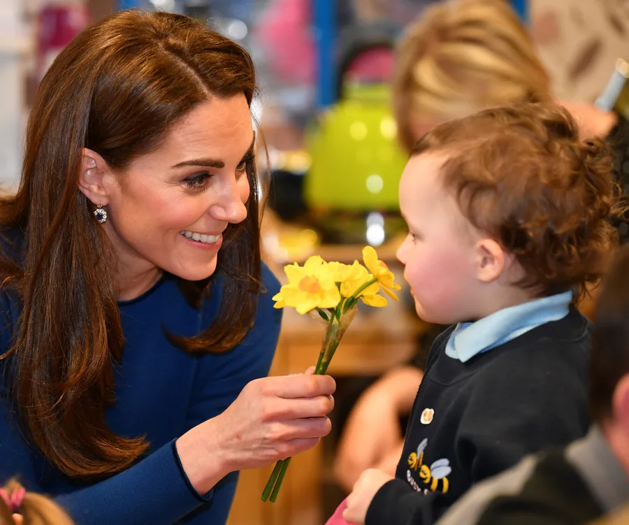 Woman smiling and offering yellow flowers to a young child.