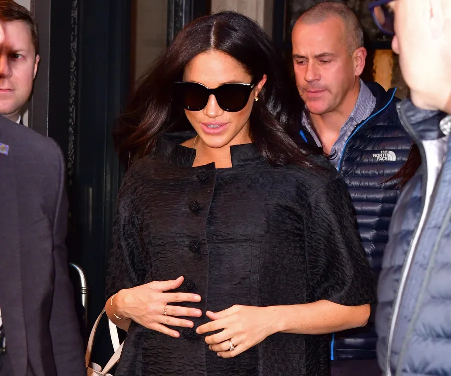 Woman in a black coat and sunglasses leaving a building, accompanied by several people.