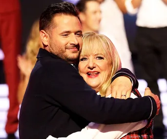 Two people embracing warmly on the set of a reality TV dance competition.