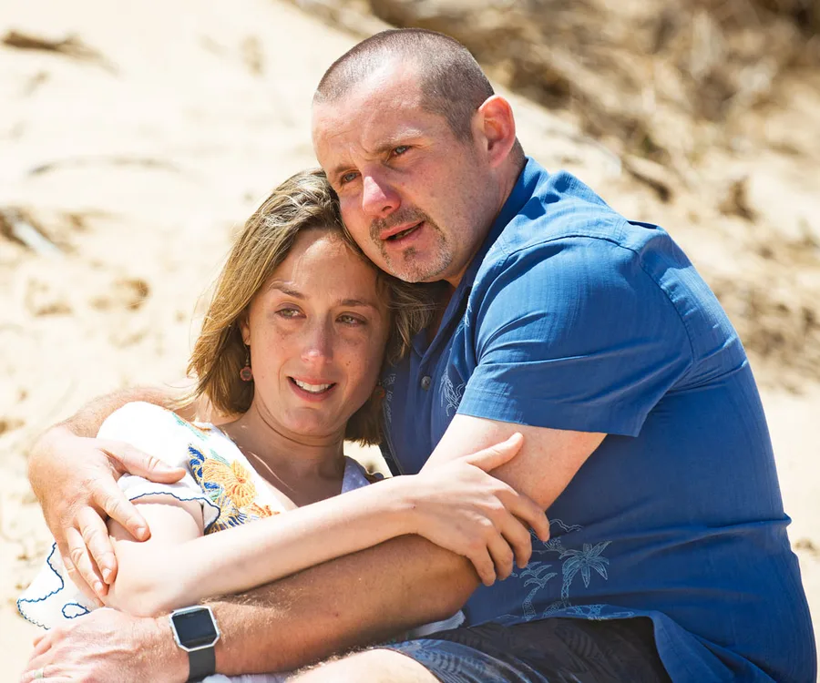 A couple embracing tenderly on a sandy beach, expressing comfort and closeness.