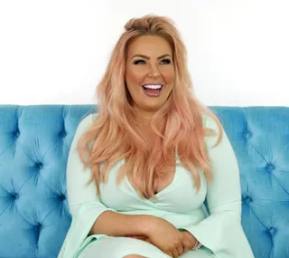 Woman with long pink hair and mint dress sitting on a blue couch, smiling broadly.