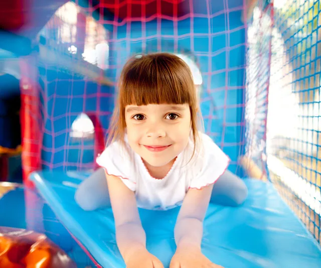 A child playing in a colorful indoor play structure, smiling at the camera.