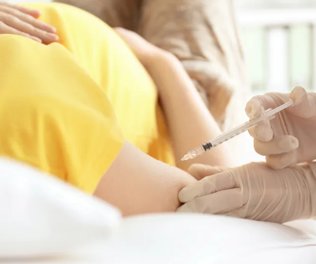 A pregnant woman receives a vaccination in her arm from a healthcare professional wearing gloves.