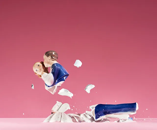 A shattered porcelain figurine of a kissing couple against a pink background.