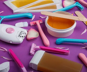 Various hair removal tools and wax on a purple background with rose petals.