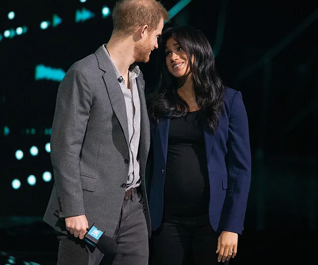 A couple stands on stage, smiling at each other, one holding a microphone with a "WE" sticker.