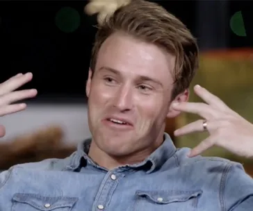 A man in a denim shirt gestures animatedly during a conversation, with a playful expression on his face.
