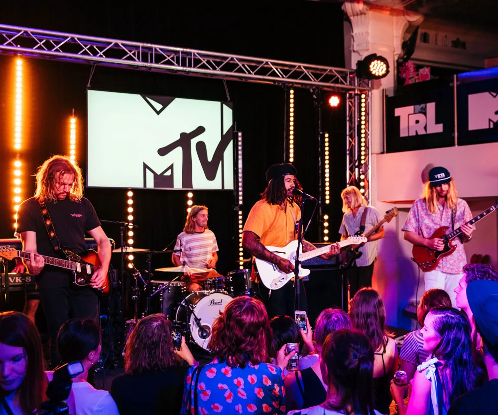 Band performing live at MTV TRL Australia, with five musicians on stage and an audience watching.