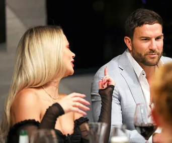 Woman gestures animatedly while talking to a man in a gray suit during a dinner conversation.