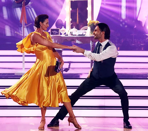 Dancers perform on "Dancing with the Stars," with the woman in a flowing yellow dress and the man in a vest and tie.