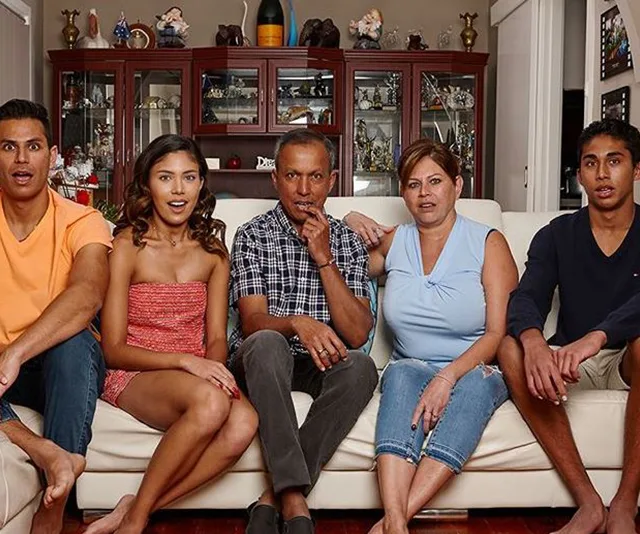 Family sitting on a couch in a living room, watching television with surprised expressions.