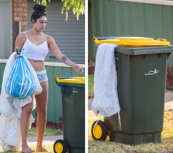 Woman in white tank top and shorts disposing of lace clothes in a yellow-lid trash bin outside.