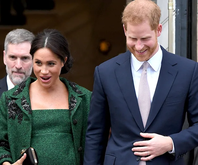 Two people smiling and walking outside a building, with one in a green outfit and the other in a suit and tie.