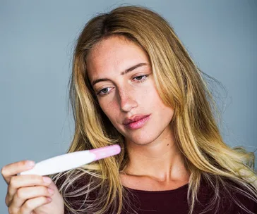 Woman with long hair looking pensively at a pregnancy test in her hand.