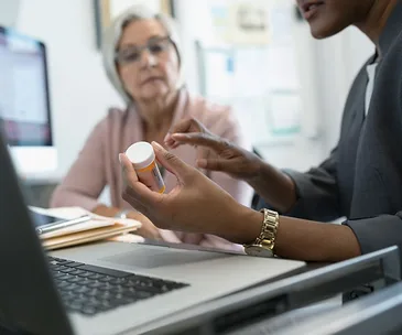 Healthcare professional explaining medication to a senior woman in an office setting.