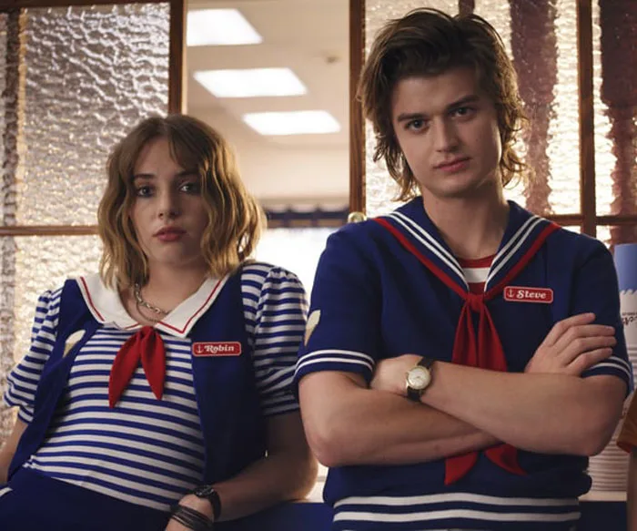 "Two characters in navy sailor uniforms with 'Robin' and 'Steve' nametags stand in front of a store counter."