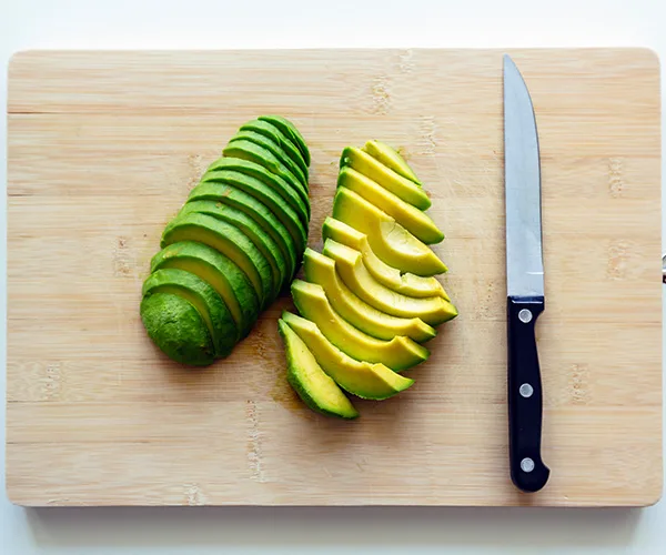 Sliced avocado on a wooden cutting board beside a knife.