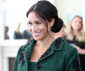 Smiling woman in a green embellished coat at an indoor event with people in the background.